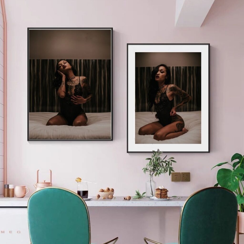 Two framed photos of a person in black lace attire on a bed, displayed in a stylish room with green chairs, a pink wall, and plants. The scene is elegant and moody.